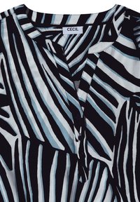 Blouse rayée noire et blanche avec col en V boutonné, présentant des lignes verticales et diagonales irrégulières et une étiquette de marque cousue "CECIL."