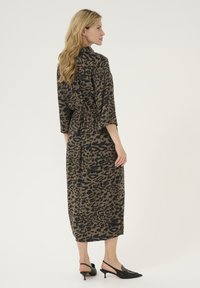 Leopardprint jurk in bruin en zwart, met driekwartmouwen, een elastische taille en een lengte tot halverwege de kuit. Ggedragen met zwarte slingback schoenen.