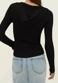 Czarna, prążkowana, długosleeve'owa bluza z kapturem o luźnym kroju, w połączeniu z jasnoniebieską spódnicą dżinsową z tylnymi kieszeniami.