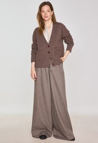 Cardigan en tricot marron avec un col en V, des poignets côtelés et deux poches avant. Associé à un pantalon large marron clair.