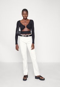 Top preto de manga longa com um corte e um acento circular, combinado com calças brancas de cintura alta e sandálias pretas chunky.