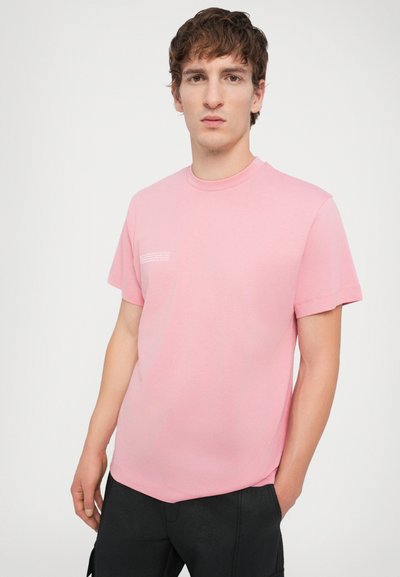 T-shirt en coton rose clair avec un col rond, des manches courtes et un petit détail de texte imprimé en blanc sur la zone gauche de la poitrine.