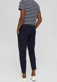 Granatowe chinosy o zwężanym kroju, wykonane z gładkiego materiału. Posiadają boczne kieszenie oraz tylną kieszeń zapinaną na guzik, zestawione z białymi trampkami.