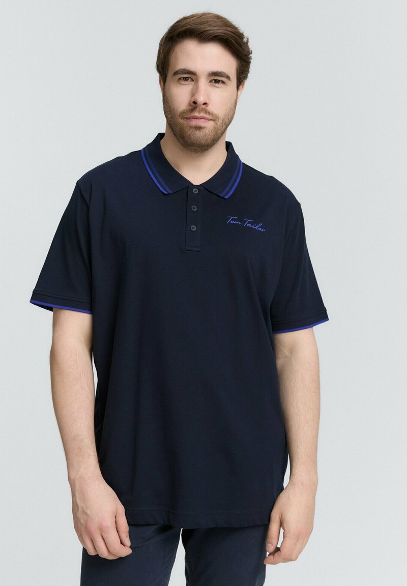 Marineblauwe polo met korte mouwen, contrasterende blauwe accenten op de kraag en mouwen, voorzien van een knoopsluiting en geborduurd logo.