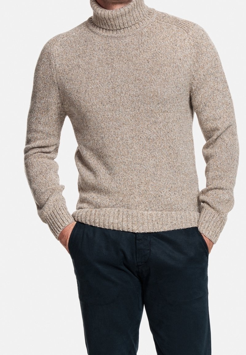 Béžový pletený rolák se žebrovanými manžetami a lemem, s texturovaným vzorem a volným střihem, nošený s tmavě modrými kalhotami.