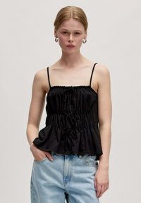 Zwarte peplum top van lichtgewicht stof met verstelbare straps, gerimpelde bh en strikdetail aan de voorkant. Gepaard met lichtblauwe spijkerbroek.