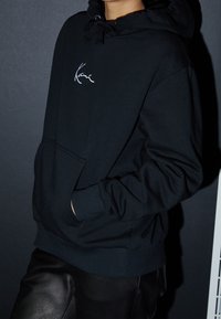 Czarna bluza z kapturem wykonana z mieszanki bawełny, z regulowanym kapturem, przednią kieszenią i haftowanym logo. Stylizowana z czarnymi skórzanymi spodniami.