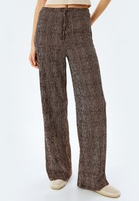 Brede broek van gestructureerde bruine stof met verticale witte strepen. Kenmerkt zich door een trekkoord in de taille en een ongecontroleerde pasvorm.