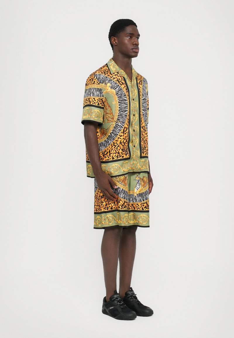 Korte mouwen shirt en shorts set in oranje, groen en zwart met patronen van dierenmotieven en gedetailleerde versieringen. Gemaakt van lichtgewicht stof.