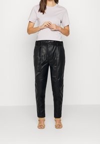 Zwarte leren broek met hoge taille, een ceintuur in de taille en een taps toelopend ontwerp. Gepaard met een lichtpaarse T-shirt met korte mouwen.