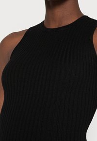 Débardeur noir côtelé présentant une coupe ajustée, un col montant et une coupe sans manches, mettant en avant un tissu texturé et des lignes épurées.