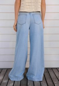 Vaqueros de pernera ancha de un azul claro, hechos de mezclilla, con dos bolsillos traseros y un dobladillo cosido. Llevados con un top corto de punto beige.