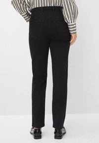 Jeans in denim nero con una vestibilità dritta, caratterizzati da una vita alta, due tasche posteriori e cuciture strutturate. Indossati con scarpe nere.