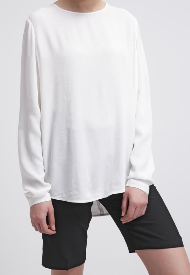Vit långärmad blus med rund halsringning, slät textur och avslappnad passform, tillsammans med svarta shorts med en enkel design.