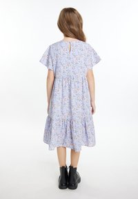 Helles blaues Blumenkleid mit kurzen, flatternden Ärmeln, schichteter Rock und Schlitzdetail im Rücken. Kombiniert mit schwarzen Knöchelstiefeln.