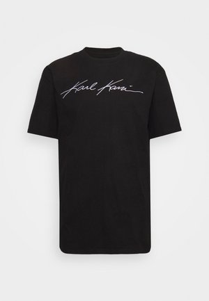 T-shirt noir à manches courtes avec logo « Karl Kani » en écriture cursive blanche centré sur la poitrine, col rond et coupe décontractée.