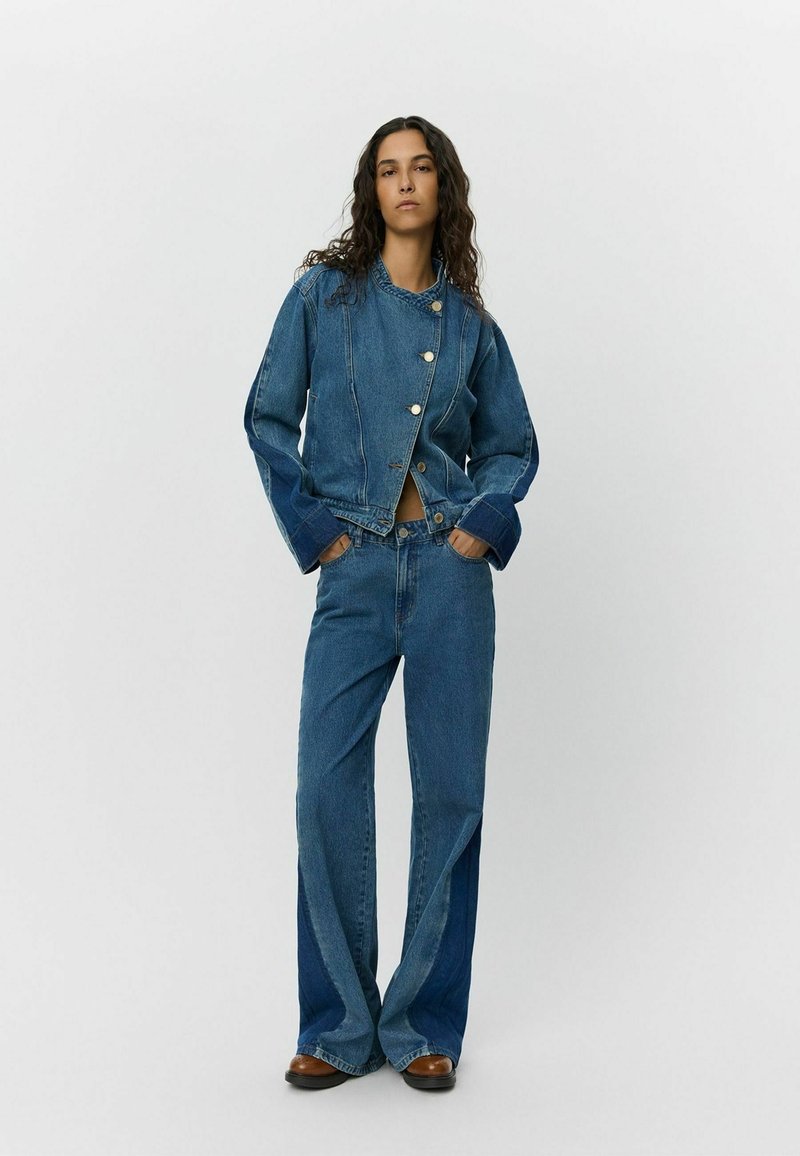 Giubbotto in denim con fit corto, chiusura a bottoni e maniche a contrasto. Abbinato a jeans a vita alta e gamba ampia con diverse tonalità di blu.