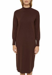 Robe tricotée marron avec un col montant, des manches longues et une coupe droite. Le tissu semble lisse avec une texture subtile. Longueur jusqu'au genou.