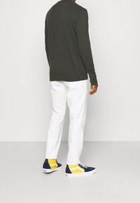 Haut à manches longues vert foncé avec un col rond, pantalon blanc et baskets bleu marine avec des accents jaunes. Texture lisse partout.