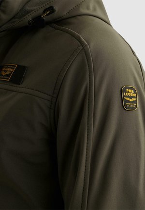 Mouw van olijfgroene jas met gestikte naden, zwarte en gele PME Legend American Classic-logopatch op de bovenarm, en een detail van een verstelkoord aan de capuchon.