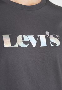 Pilkos medvilnės marškinėliai su dideliu holografiniu "Levi's" logotipu krūtinėje. Minkšta tekstūra ir klasikinis apvalus kaklas.