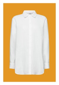 Chemise blanche à boutons, en tissu texturé, avec un col pointu et des manches longues, présentée sur un fond orange.