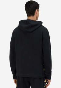 Felpa nera con una vestibilità comoda, dotata di cappuccio regolabile e dettagli dorati sui lati. Tessuto morbido con una texture liscia.