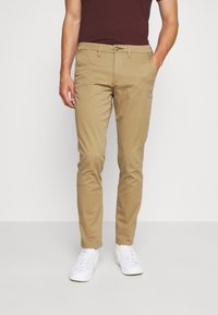 Khaki broek met een slim fit, gemaakt van katoen, met voorzakken, een traditionele riemlus en een knoopsluiting. Gepaard met witte sneakers.