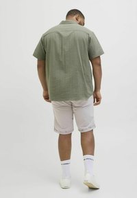 Majica kratkih rukava maslinasto zelene boje s teksturiranim uzorkom, kombinirana s svijetlosmeštim šortsevima. Bijele čarape s crnim tekstom i bijele tenisice.