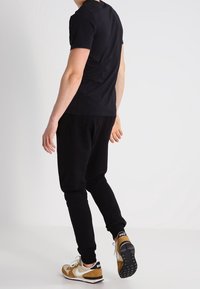 Camiseta negra ceñida, joggers negros y zapatillas beige con acentos negros. Tejido suave, corte casual y detalles en contraste en los zapatos.