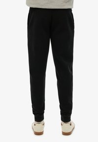 Zwarte trainingsbroek gemaakt van zacht materiaal, met zijzakken, conische pijpen en ribgebreide boorden, gecombineerd met witte sneakers.