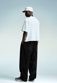 Hvid, kortærmet t-shirt og sorte fløjlshose, med en beige og maroon kasket. Grå sneakers med subtile designdetaljer.
