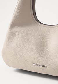Sac à main en cuir beige avec une finition texturée, une forme arrondie et un logo "MICHAEL KORS" en argent. Bords intérieurs lisses.