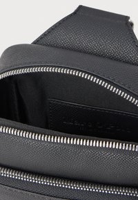 Černý texturovaný batoh se stříbrným zipem, který má prostorný vnitřek a kapsu na štítek. Materiál je syntetický a hladký.