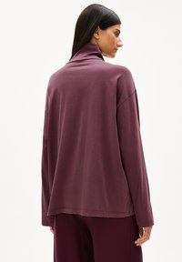 Langärmliges Pullover-Top in tiefem Burgunderrot mit einem hohen Kragen und lockerer Passform. Weicher Stoff mit glatter Textur und minimaler Naht.