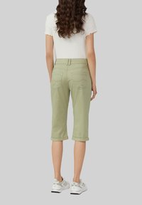 Jasnozielone spodnie capri z podwiniętymi mankietami, z tylnymi kieszeniami ozdobnie przeszytymi, w zestawie z białym prążkowanym topem i sportowymi butami.