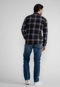 Camisa de franela a cuadros en azul marino, gris y marrón; de manga larga; ajuste relajado; textura notable. Combinada con vaqueros azules y zapatillas blancas.