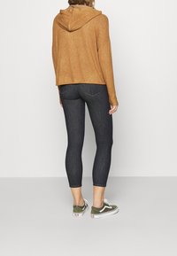 Felpa cappuccio marrone, jeans skinny scuri e sneakers verdi. Vestibilità rilassata con tessuto texturizzato e dettagli di cucitura visibili.