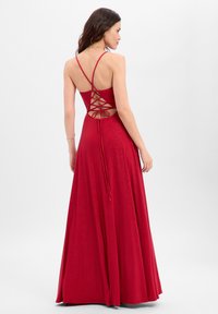 Rode jurk met een nauwsluitend lijfje, een kruisvormig rugontwerp en een volle, vloeiende rok. Gemaakt van glinsterende stof, met verstelbare bandjes.