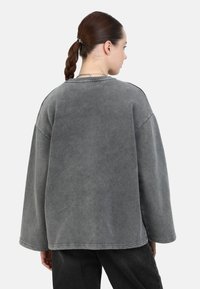 Overmaatse grijze sweatshirt met een ronde halslijn, verlaagde schouders en zichtbare stiksels. Zachte textuur met een vervaagde afwerking.