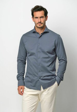 Langærmet skjorte med knapper i skifergrå, glat stof, med klassisk krave og kontrastknapper. Båret med lyse bukser.