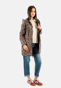 Abrigo de leopardo con cremallera en el frontal, combinado con un suéter crema y vaqueros azules con dobladillo. Un look informal complementado con zapatillas rojas y blancas.