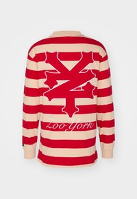 Long-sleeve shirt with red and beige horizontal stripes, featuring a large red logo and "Zoo York" in white on the back.