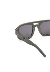 Grijze zonnebril met een matte afwerking, voorzien van gouden accenten, in een gedurfde rechthoekige vorm, en donkere getinte lenzen. Stevige zijkanten met groeven.