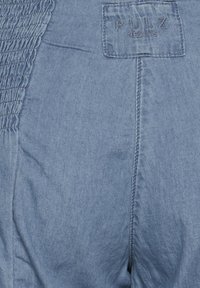 Traperice u svijetloplavoj boji, s naboranom teksturom sa strane i prošivenom oznakom "PULZ JEANS" na pojasu.