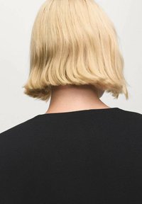 Capelli biondi corti con una trama ondulata, visti da dietro. Il soggetto indossa un semplice top nero con scollo rotondo. Design minimalista.