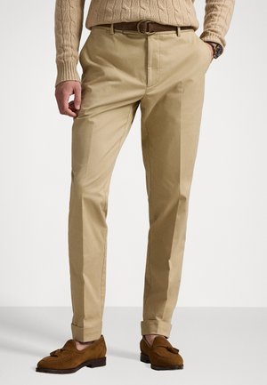 Beige skreddersydde bukser med en glatt tekstur, med frontfold og oppbrettede ermer. Kombinert med brune semskede loafers.