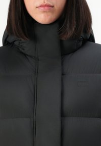 Black puffer jacket with a high collar and horizontal seams. Smooth material with a minimalist logo detail on the chest.