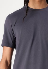 Tamsiai pilka, apvaliu kaklu t-shirt, pagaminta iš minkštos medžiagos. Trumpomis rankovėmis, su tvarkingais siūlais ir lygia tekstūra. Tinkanti prie kūno.