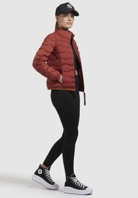 Rode gewatteerde jas met hoge kraag, zwarte leggings en zwarte hoge sneakers met witte zolen. Geen zichtbare patronen of accenten.
